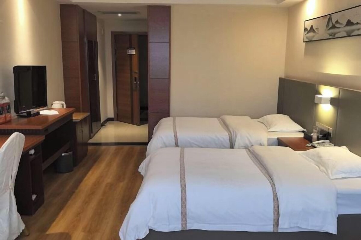 Ein Hotelzimmer mit Schreibtisch, zwei Betten, einem Fernseher und einer Tür zu einem weiteren Raum.