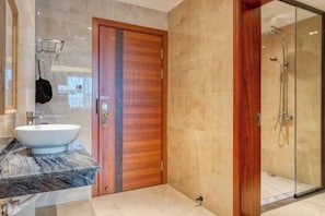 Ein modernes Badezimmer mit Marmorwaschtisch, Holztür und einer Duschkabine aus Glas.
