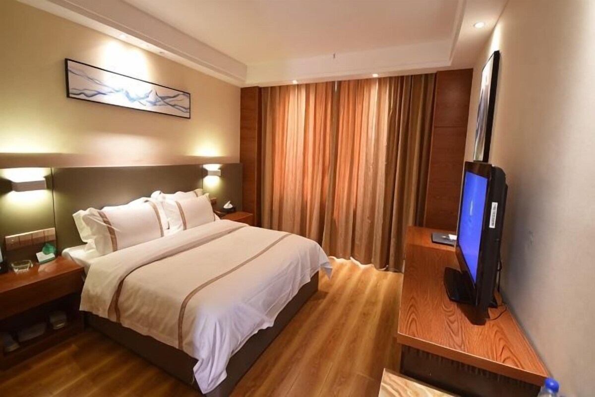 Quarto de hotel com cama, luminárias de cabeceira, TV de tela plana e cabeceira de madeira.