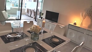 A modern dining area with a glass table set for two, a TV, and a candle on a side table.