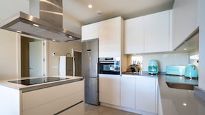 A modern kitchen with white cabinets, a stainless steel range hood, a built-in oven, a refrigerator, and vintage-style appliances.