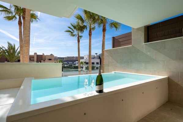 A rooftop pool with a bottle of champagne, palm trees, and a clear sky.