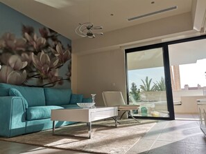 A modern living room with a teal sofa, a white coffee table, and a large window with a view of palm trees. - Holiday Apartment "Azalea 471" with Pool, Terraces & Wi-Fi (La Cala de Mijas)