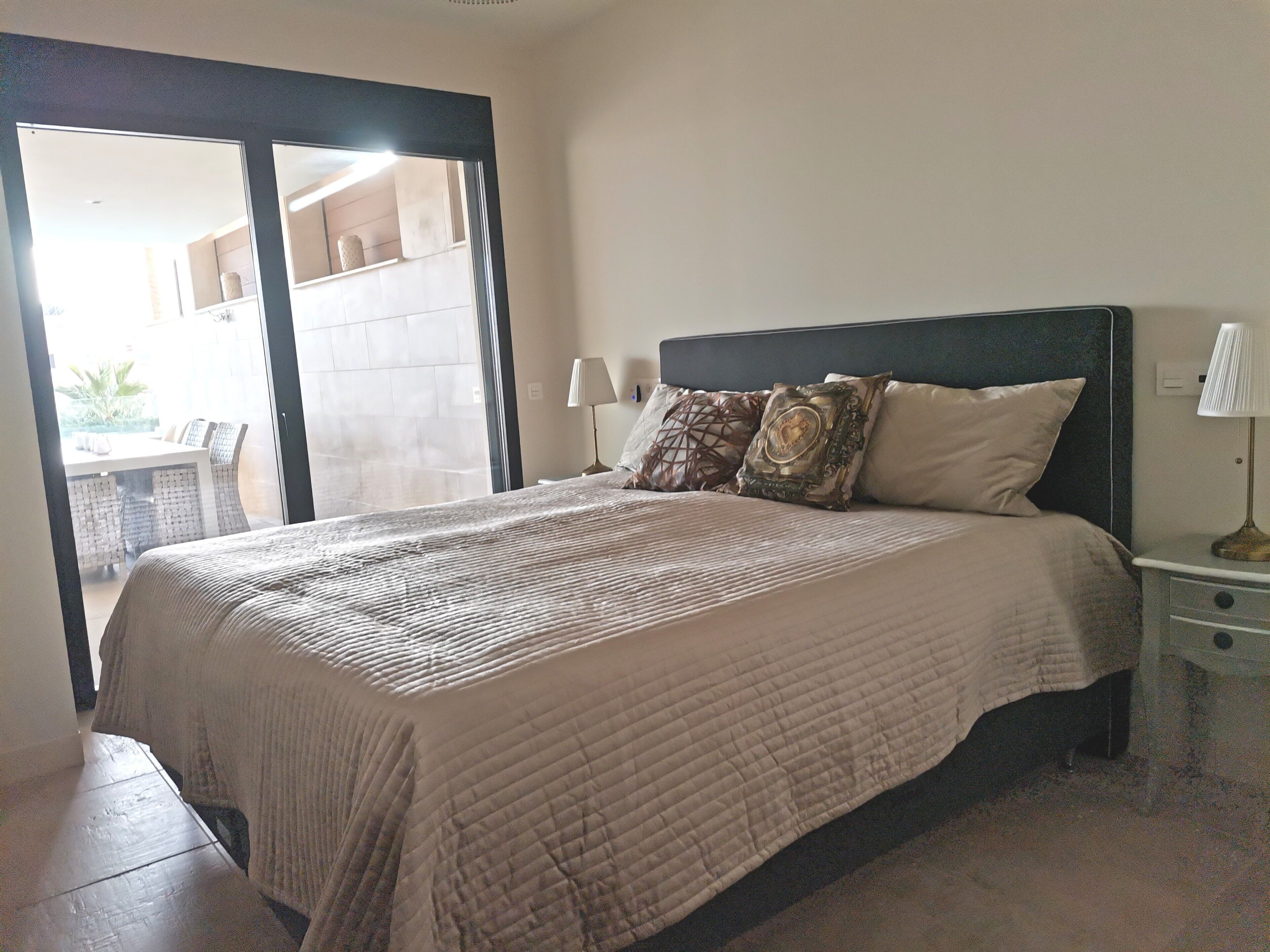 Un dormitorio con cama, mesita de noche, lámpara y vistas a un espacio exterior.
