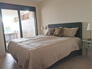 A bedroom with a bed, a nightstand, a lamp, and a view of an outdoor area.