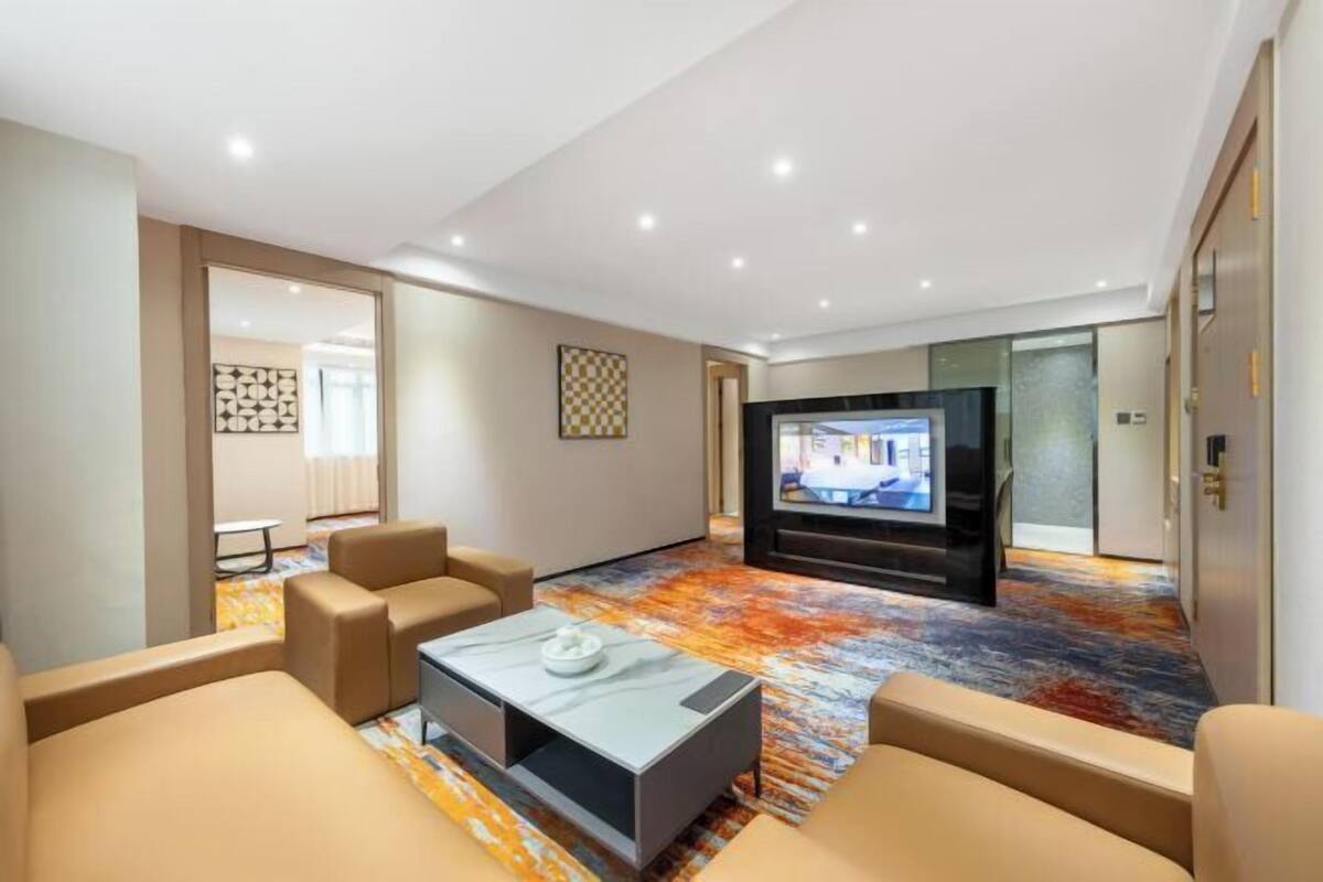A hotel room with a sofa set, a flat-screen TV, and a patterned carpet.