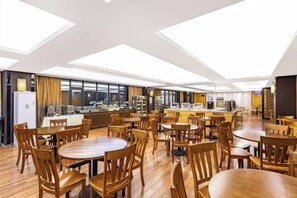 Un grand espace à manger avec plusieurs tables et chaises, une cuisine à l’arrière-plan et des fenêtres de toit au plafond.