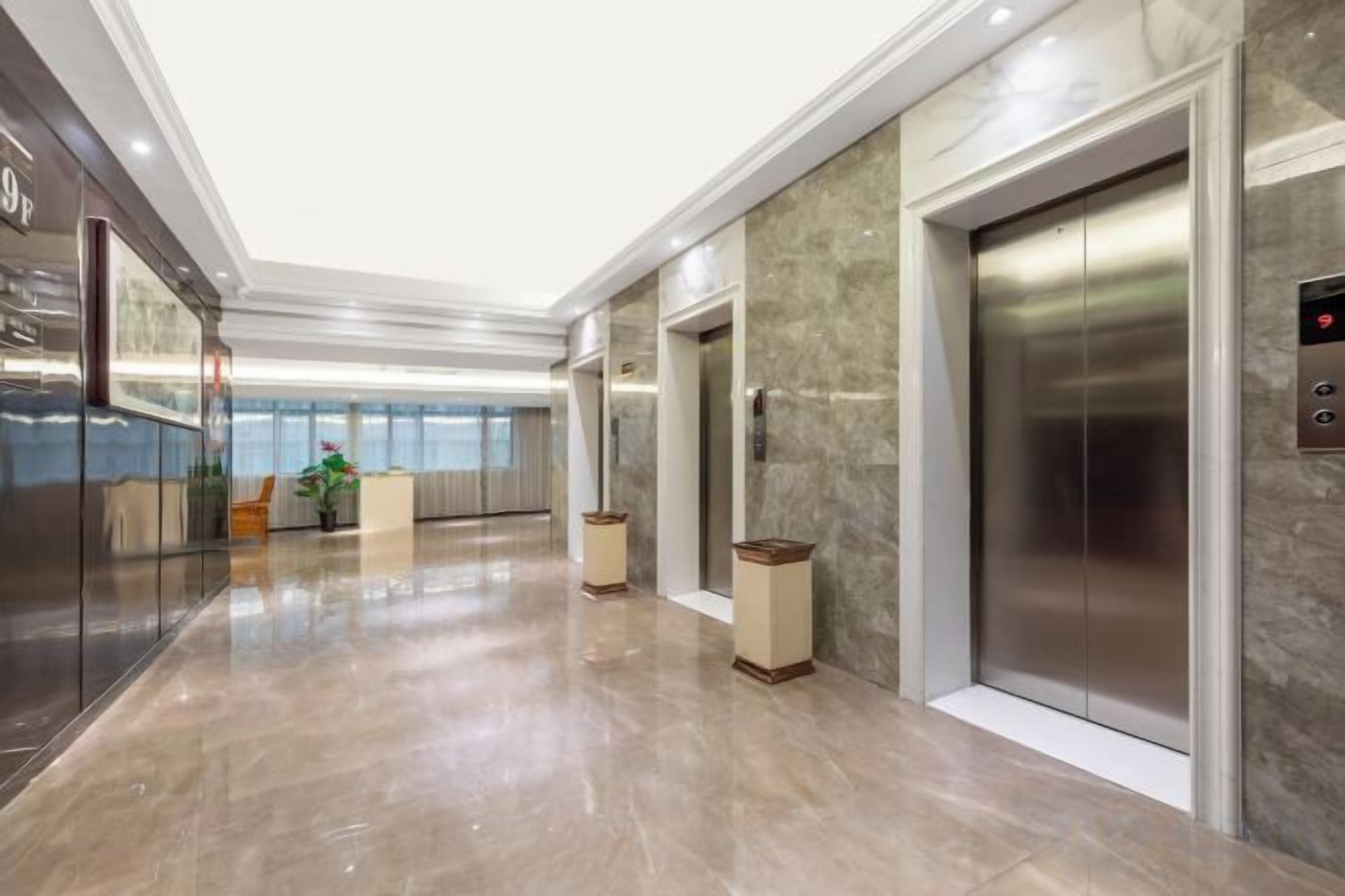 A modern elevator with a metallic finish, a marble wall, and a glass elevator door.