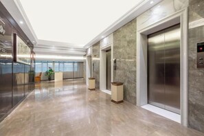 A modern elevator with a metallic finish, a marble wall, and a glass elevator door. - Huanyang Oriental Hotel (Shantou)