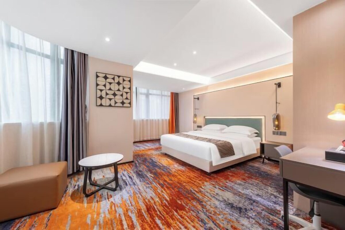 Une chambre d’hôtel avec un lit, un bureau, une chaise, une petite table et une fenêtre avec des rideaux.