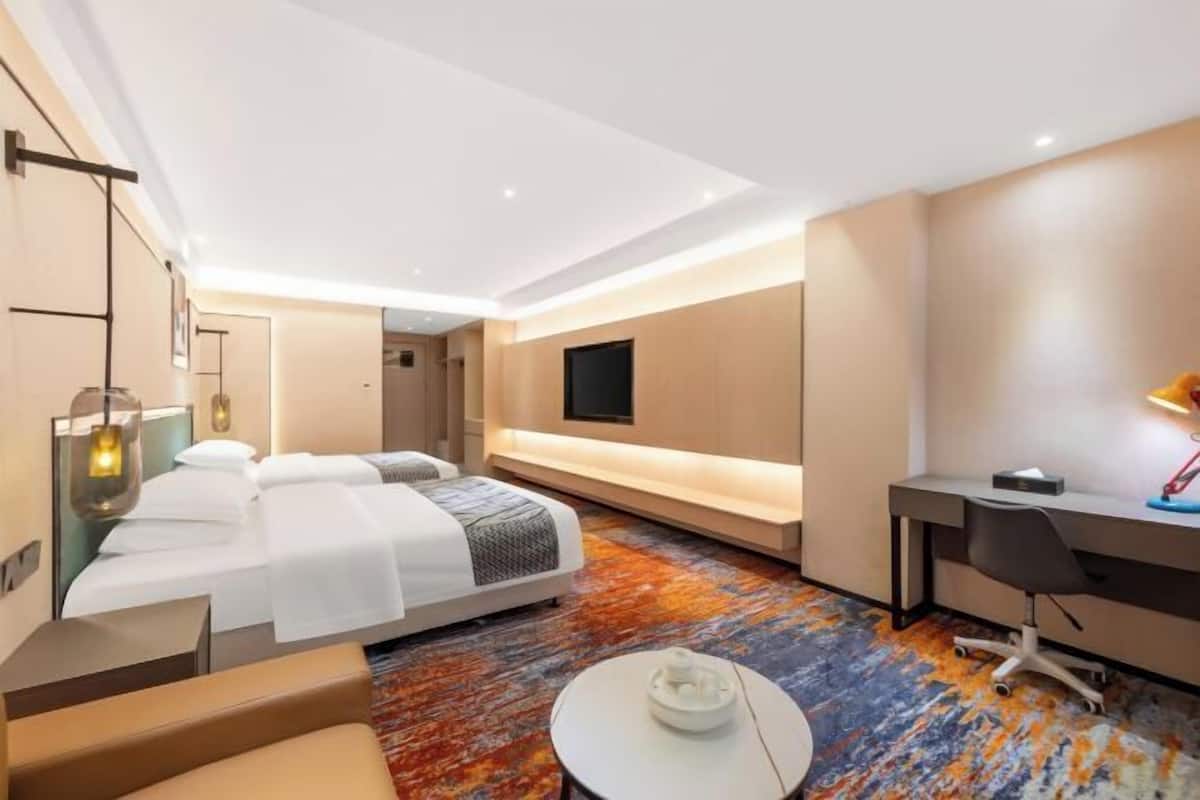 A modern hotel room with a bed, desk, and seating area.