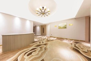 A hotel lobby with a reception desk, a patterned carpet, a chandelier, and a painting on the wall. - Huanyang Oriental Hotel (Shantou)