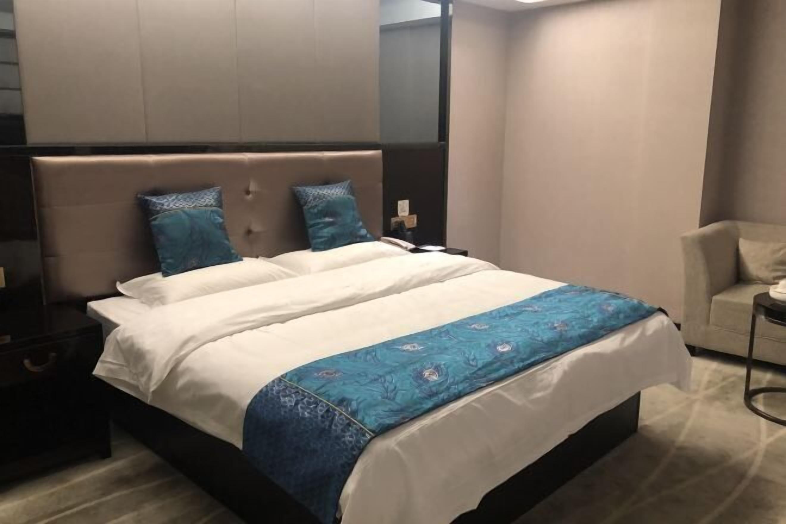 A modern hotel room with a large bed, two pillows, a bedside table, and a chair.