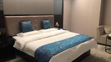 A modern hotel room with a large bed, two pillows, a bedside table, and a chair.