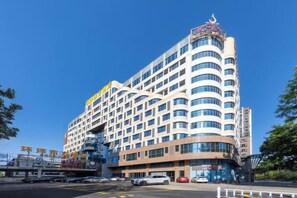 Un hôtel à plusieurs étages, doté d’un design moderne, avec une entrée imposante et un grand espace de stationnement à l’avant.