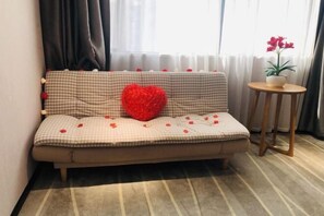 Una habitación acogedora con un sofá estampado de cuadros, un cojín rojo con forma de corazón y una mesita con una planta en maceta.
