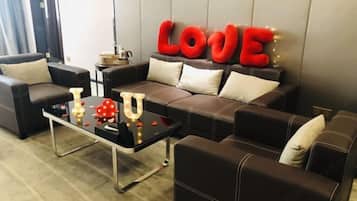 A modern living room with a sofa set, a glass coffee table, and decorative elements like red letters spelling "LOVE" and heart-shaped lights.