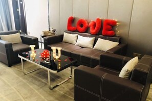 Una sala de estar moderna con un juego de sofá, una mesa de centro de vidrio y elementos decorativos como letras rojas que deletrean “LOVE” y luces con forma de corazón.