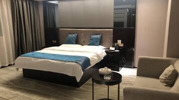 A hotel room with a large bed, a bedside table with a lamp, a small round table with a tissue box, and a sofa.