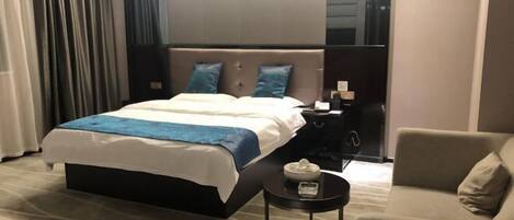 A hotel room with a large bed, a bedside table with a lamp, a small round table with a tissue box, and a sofa.