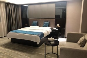 Habitación de hotel con una cama grande, una mesita de noche con lámpara, una mesita redonda pequeña con caja de pañuelos y un sofá.