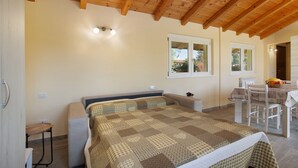A bedroom with a wooden ceiling, a bed with a checkered bedspread, a small table with a chair, and a window with a view of the outside. - Holiday Home Casina Bianca with Garden, BBQ & Wi-Fi (Lurate Cacivio)