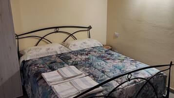 A single bed with a floral bedspread and pillows, a wooden ceiling, and a white wall.