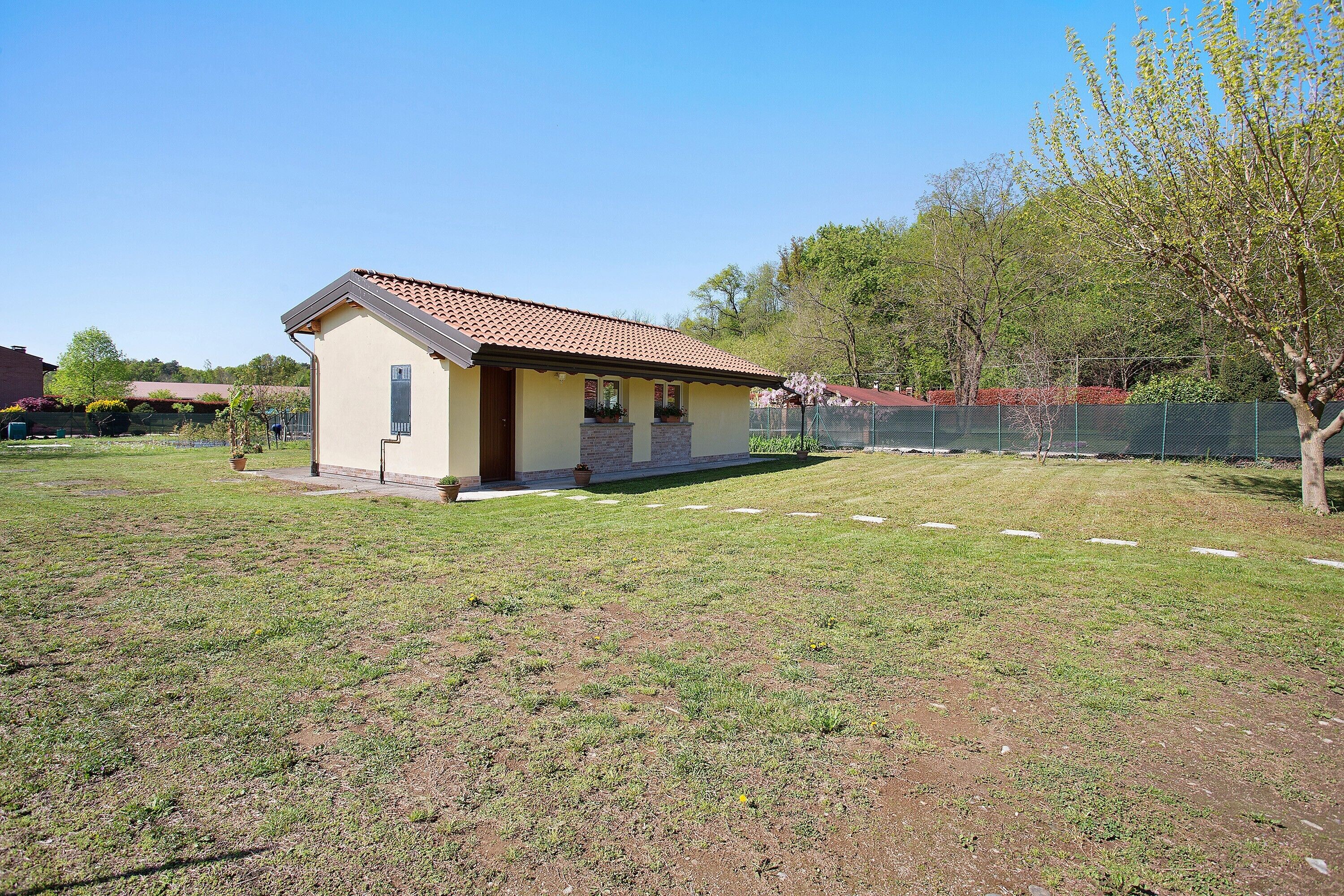 A small house with a tiled roof, a front porch, and a yard with a tree and a fence.