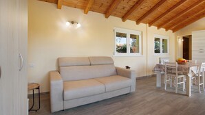 A room with a sofa, dining table, and chairs, wooden ceiling beams, and windows. - Holiday Home Casina Bianca with Garden, BBQ & Wi-Fi (Lurate Cacivio)