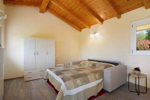 A bedroom with a bed, a wardrobe, a small table with a plant, and a window with a view of greenery. - Holiday Home Casina Bianca with Garden, BBQ & Wi-Fi (Lurate Cacivio)