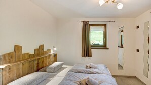 A bedroom with a wooden headboard, two beds with patterned bedding, a window with curtains, and a mirror on the wall.