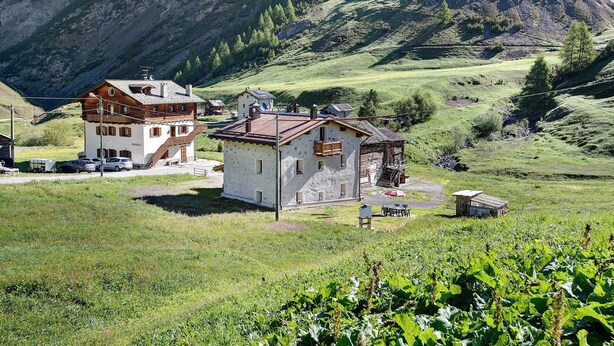 A two-story building with a sloped roof, a small attached structure, and a clear view of a mountainous landscape.