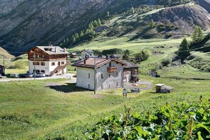 Ein zweistöckiges Gebäude mit geneigtem Dach, einem kleinen Anbau und freiem Blick auf eine Berglandschaft.
