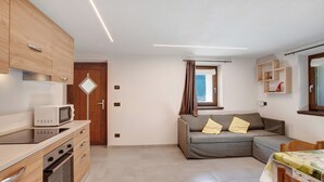 A compact living space with a kitchenette, a sofa, a dining table, and a window with curtains.