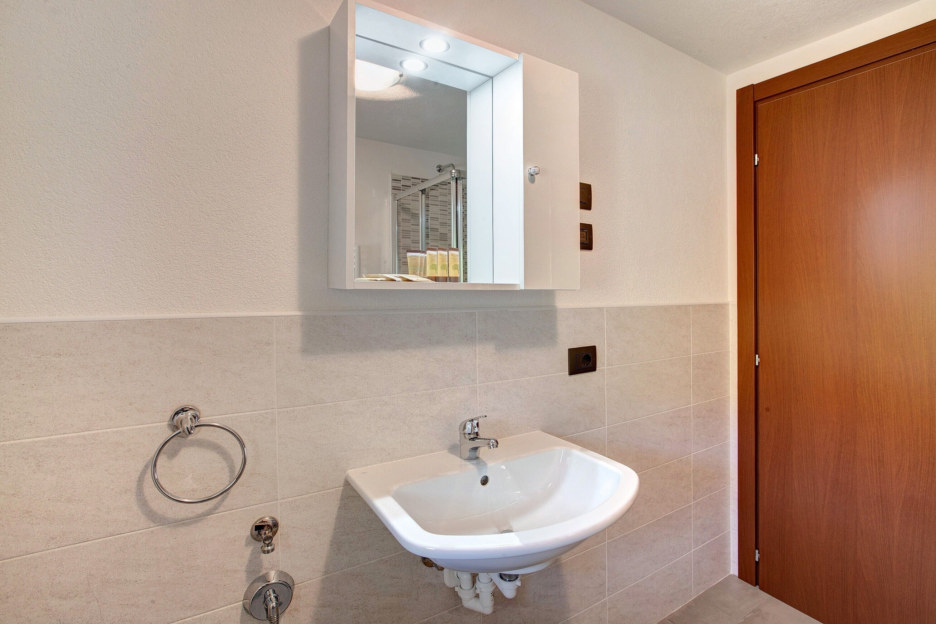 Une salle de bain avec un lavabo blanc, un miroir et une porte en bois.