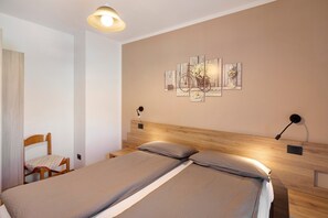 Un dormitorio con cabecera de madera, cama con ropa de cama gris, una silla y una lámpara fijada a la pared.