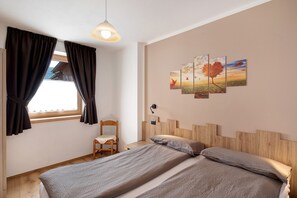Een slaapkamer met een bed, een stoel, een raam met gordijnen en een muur met drie schilderijen.