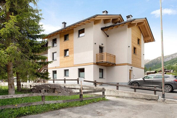 Un immeuble à plusieurs étages doté de balcons, d’un espace de stationnement et surplombant un paysage montagneux.