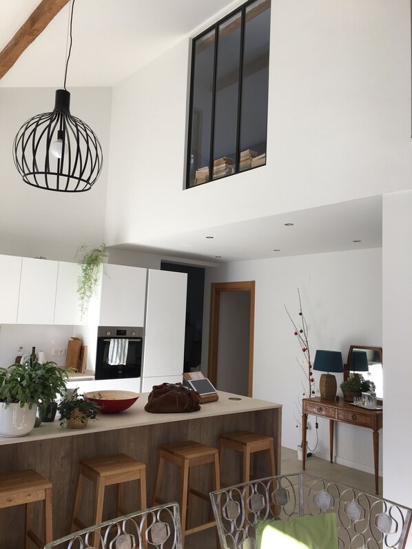A modern kitchen with white cabinets, a wooden island with stools, a hanging light fixture, and a large window. - Villa Capbreton in a quiet location, within walking distance of the beach (Capbreton)