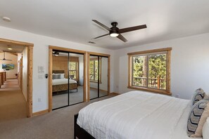 A bedroom with a bed, a ceiling fan, and large windows. - Mountain Chic by Destination Big Bear : Gorgeous Log Home Located in Castle Glen Estates! Game Room! Lake Views! (Big Bear Lake)
