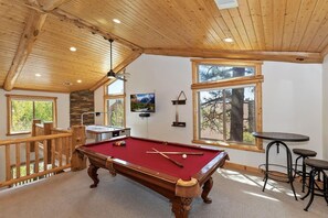 A pool table in a room with wooden beams, a stone wall, and large windows.