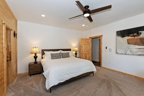 Un dormitorio con cama, mesitas de noche, ventilador de techo y una puerta.