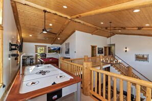 A room with a pool table, wooden ceiling beams, a staircase, and a chandelier.
