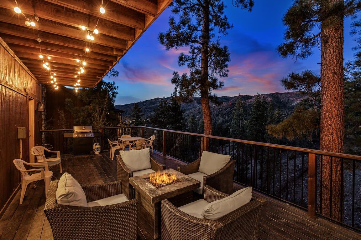 An outdoor deck with wicker furniture, a fire pit, and a view of a mountainous landscape.
