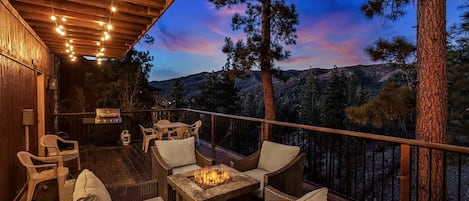 An outdoor deck with wicker furniture, a fire pit, and a view of a mountainous landscape.