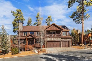 A two-story log cabin with a stone chimney, a front porch, and a garage.
