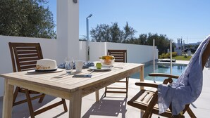 Een houten tafel met stoelen, een hoed, een glas, een fruitschaal en een smartphone.