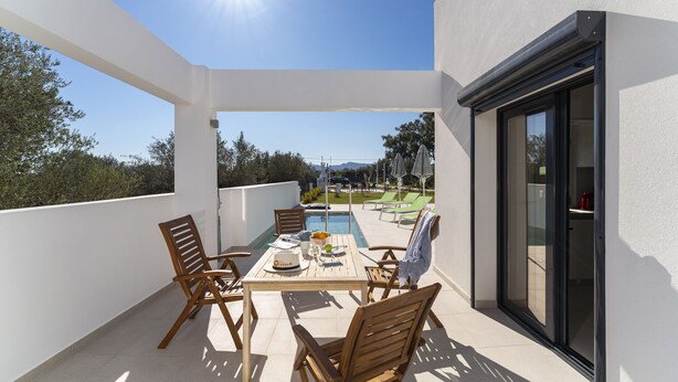 Een balkon met een eettafel, met uitzicht op een zwembad en een aangelegde tuin.