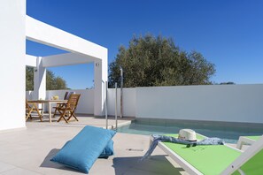 A rooftop pool area with a table and chairs, a lounge chair, and a view of the sea.