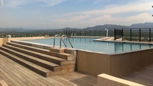 A rooftop infinity pool with a wooden deck and metal railings, overlooking a mountainous landscape.